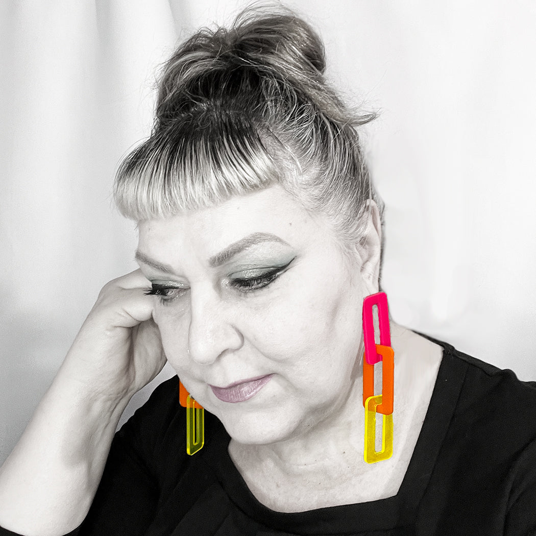 Lady wearing vibrant chunky chain link earrings, featuring bold hues of hot pink, orange and yellow to show scale.