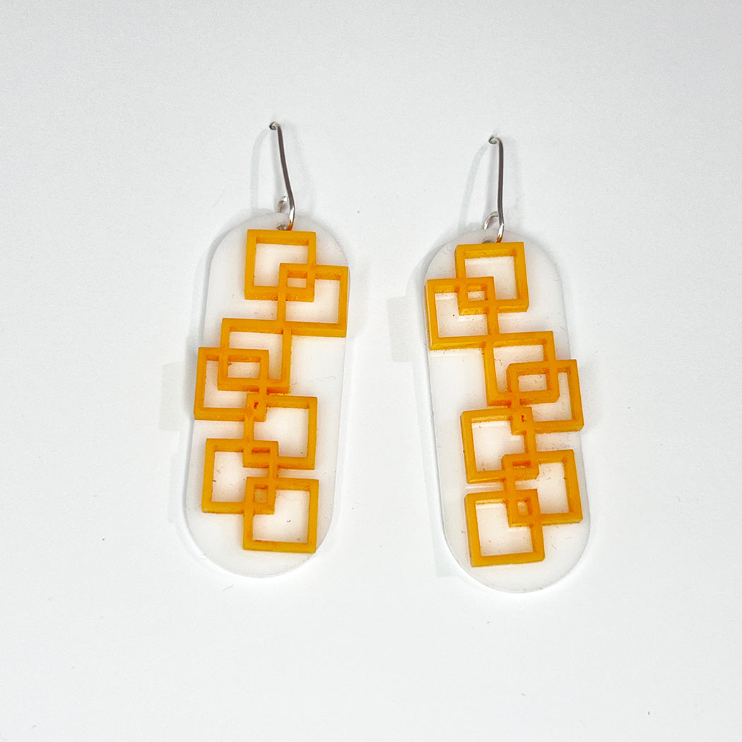 Closeup of tangerine square grid earrings in orange and white on white background from by Barbe Jewelry.