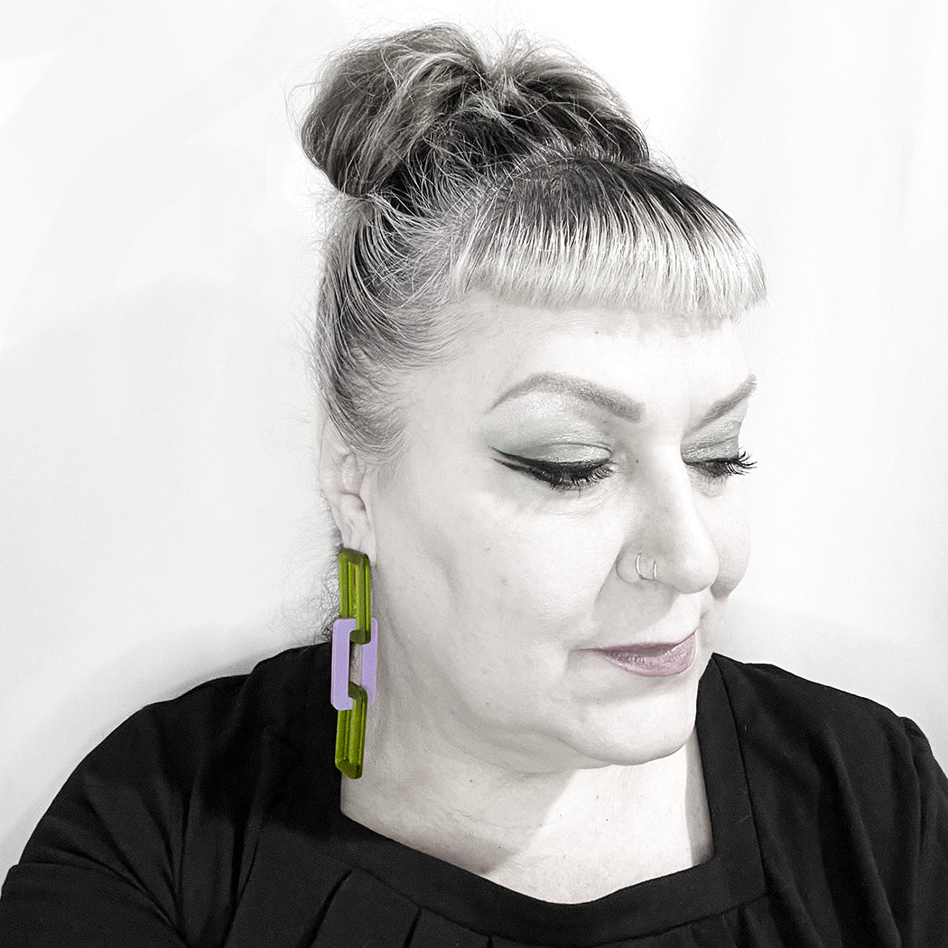 Woman showing scale of large link acrylic chain earrings in green and purple.